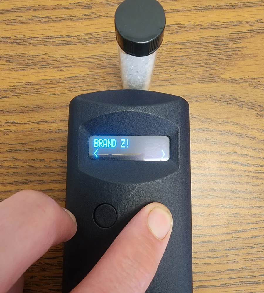 A pocket reader showing BRAND Z! next to a vial of tagged plastic pellets